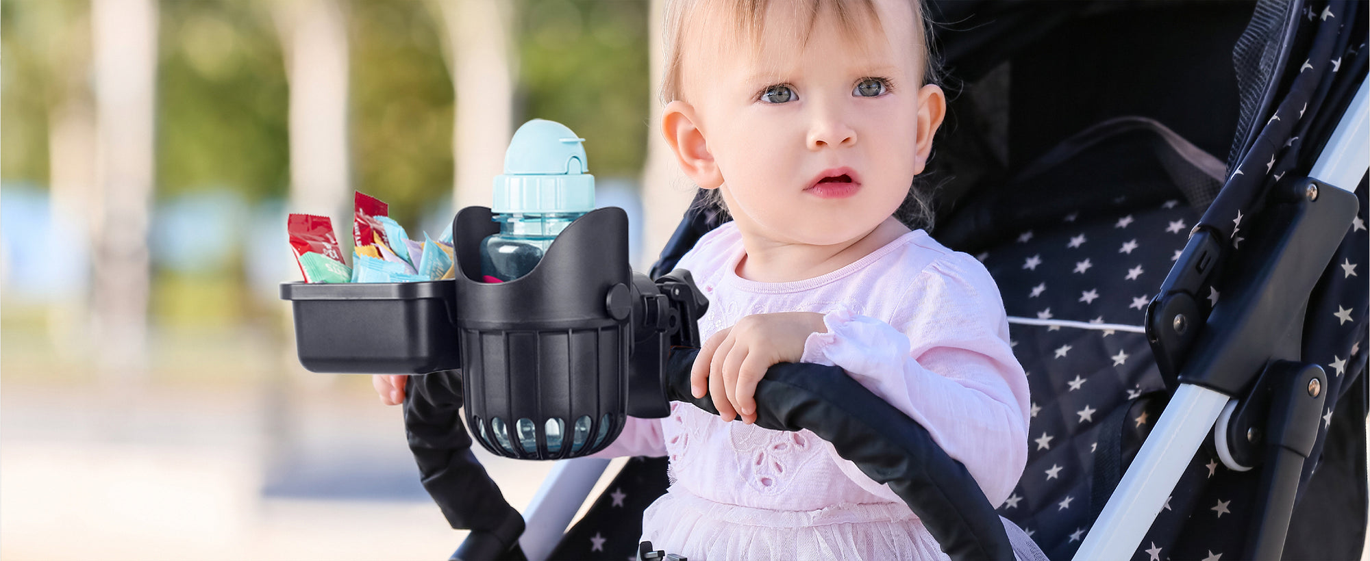 Baby in a stroller with a stroller cup holder attached outdoors