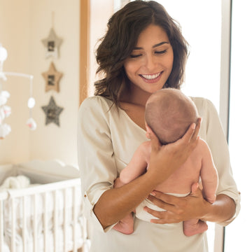 Mom holding a baby in a nursery with a crib and decorations
