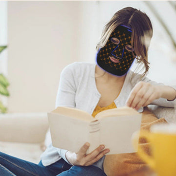 A woman wearing a led mask while reading a book indoors