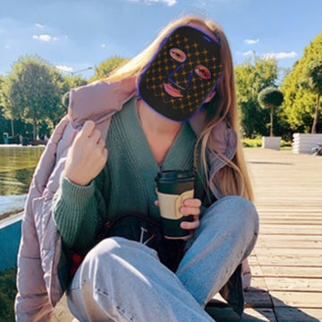 A woman wearing an LED mask and holding a coffee cup outdoors