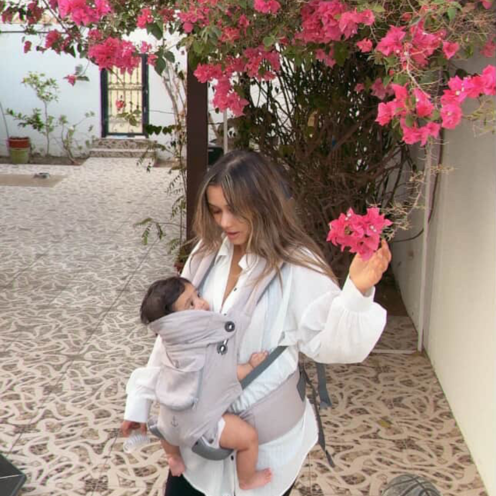 A mom holding a baby in a baby carrier holder with a floral archway in the background