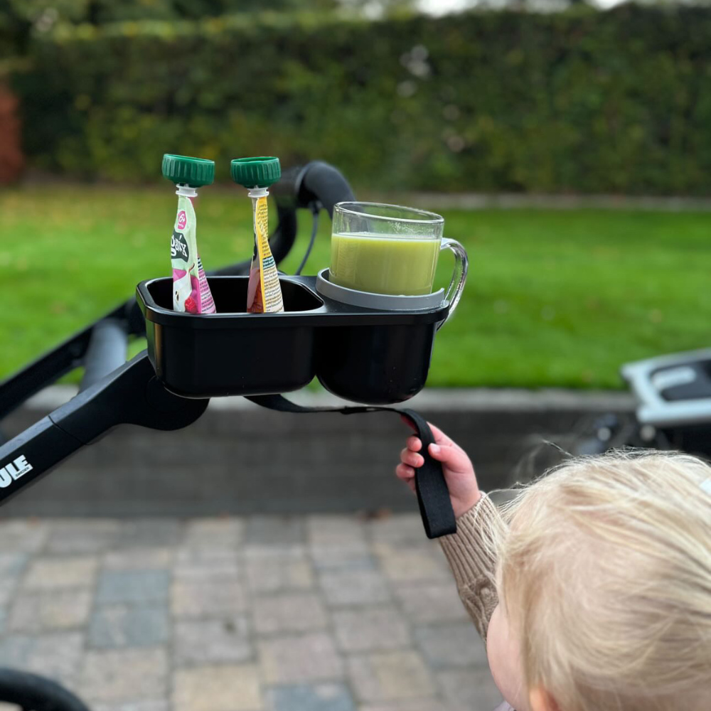 A child holds a black stroller cup holder with drinks and snacks 