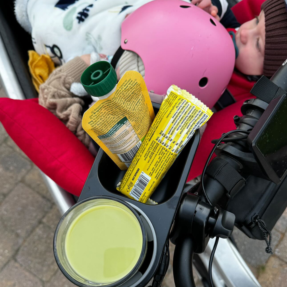 A child in a stroller with snacks and drink in a stroller cup holder attachment