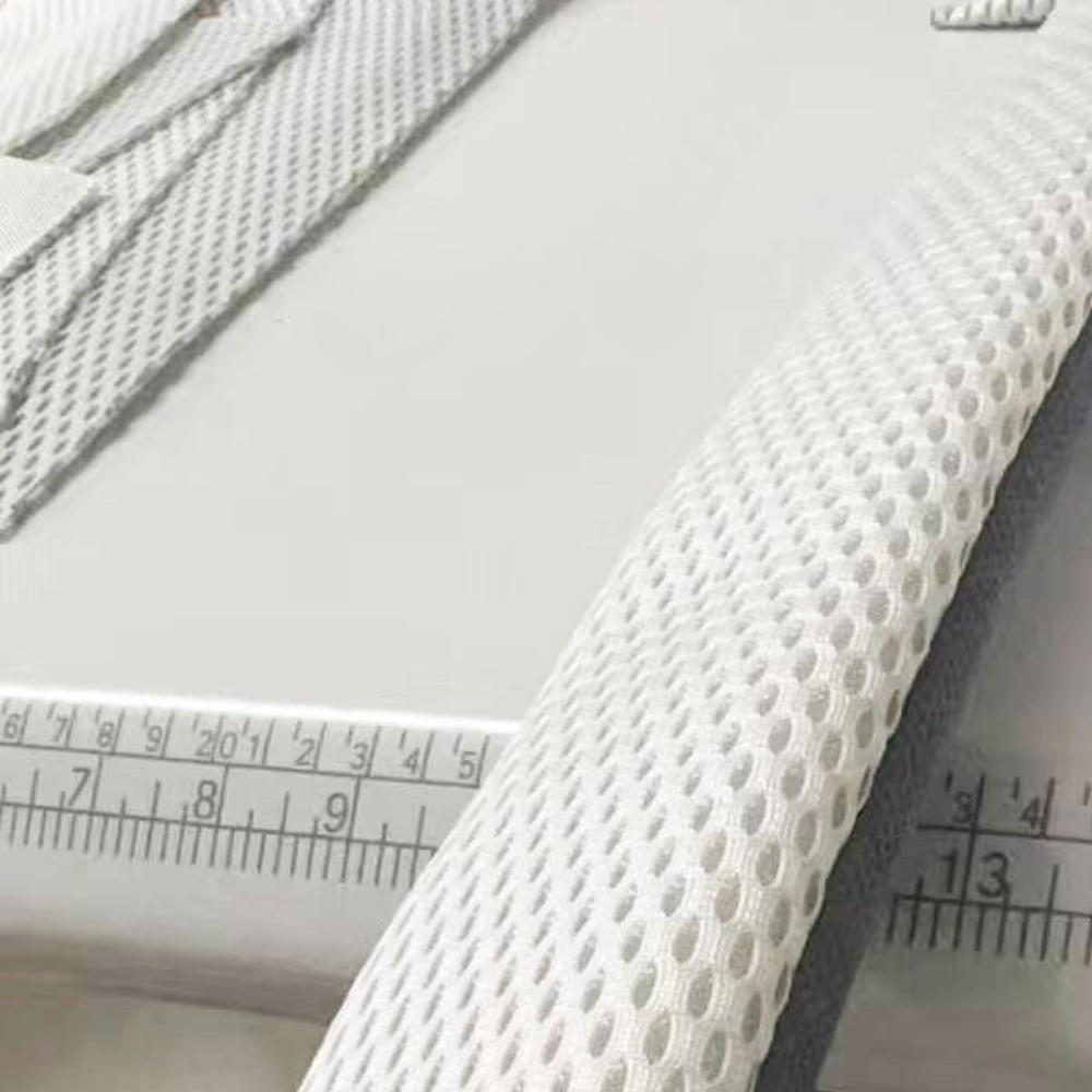 The close-up and finishes of a white textured fabric for shoulder straps of a baby carrier with a ruler for scale