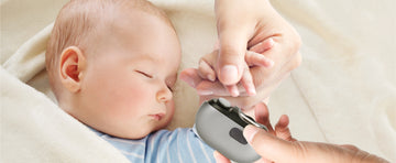 A mother gently trimming her sleeping baby’s nails with a quiet electric nail file, capturing a moment of tender care