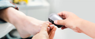 One adult using an electric nail clipper to cut other person's toe nails