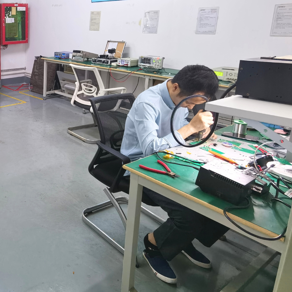 A person working on electronic components for electric nail clippers mass production at a desk in a laboratory setting
