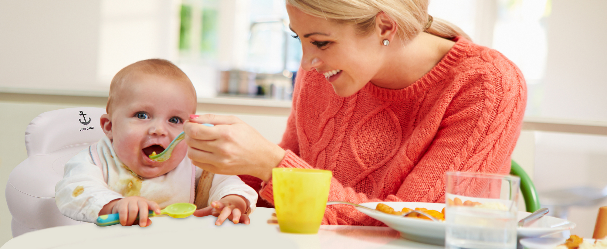 Mother feeding baby with spoon while child sits in inflatable feeding chair at home