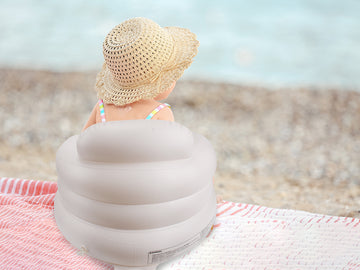 Child sitting on a beach with an inflatable seat and straw hat, looking at the ocean