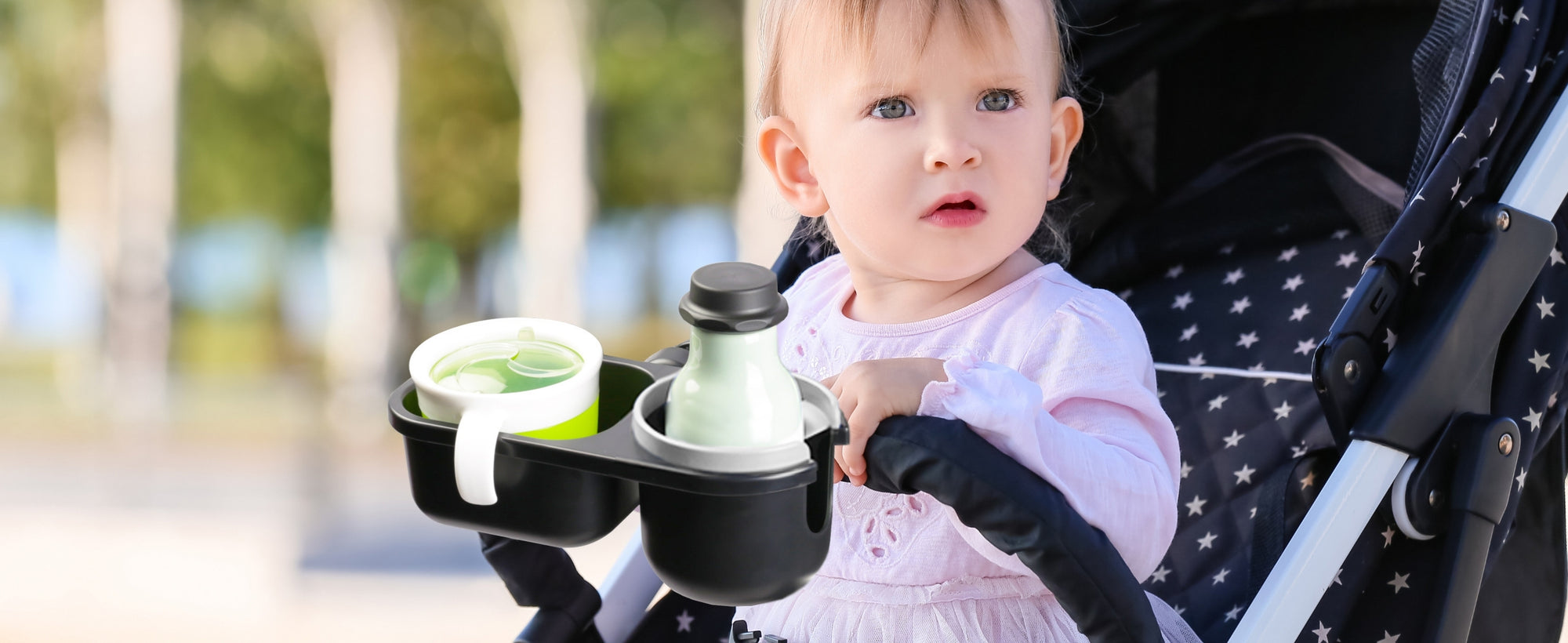 Baby in a stroller with cup holders holding drinks outdoors