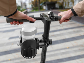 Adult holding scooter handle with attached scooter drink holder for outdoor use