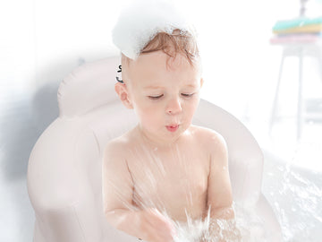 Baby taking a bubble bath in a white bathtub, playing with foam during infant bathing routine