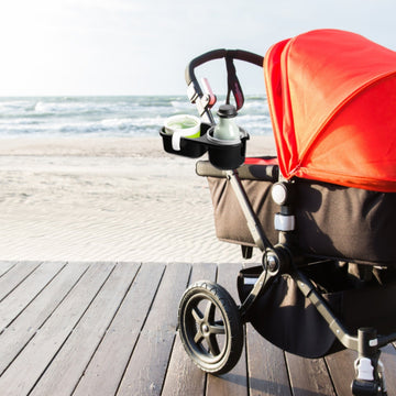 Stroller cup holders holding drinks on a wooden boardwalk by the beach