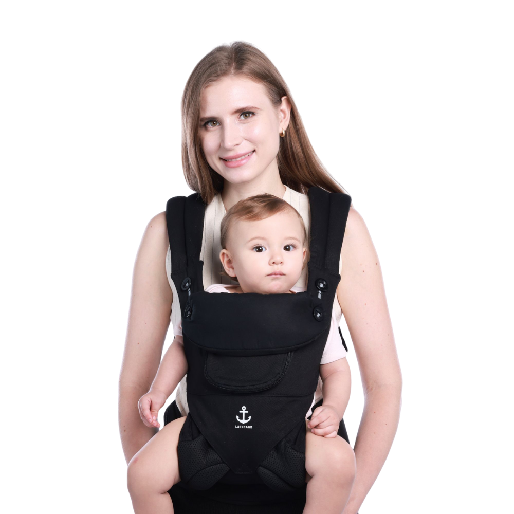 A mom holding a baby in a black ergonomic baby carrier 