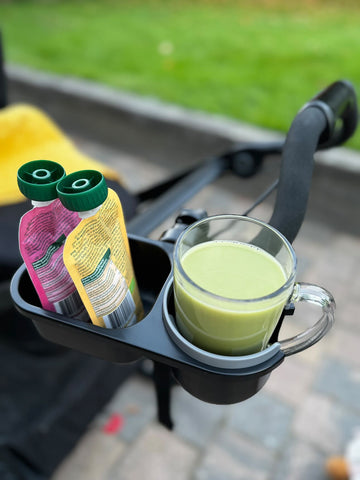 Cup holder in a stroller with juice bottles and a glass of green juice